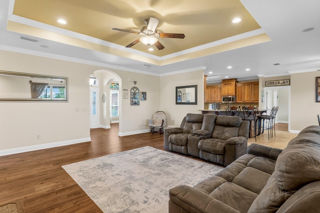 living room featuring dark hardwood / wood-style flooring, a raised ceiling, ceiling fan, and ornamental molding