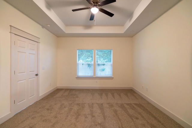 empty room with a raised ceiling, ceiling fan, and carpet