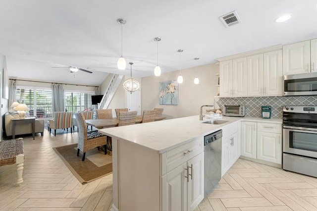 kitchen featuring light parquet flooring, appliances with stainless steel finishes, decorative light fixtures, and sink