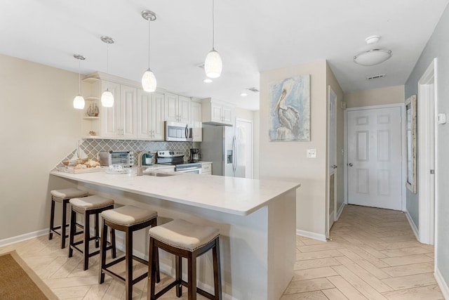 kitchen featuring pendant lighting, appliances with stainless steel finishes, kitchen peninsula, and light parquet floors