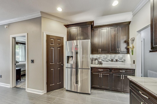 kitchen featuring decorative backsplash, light stone countertops, dark brown cabinets, crown molding, and stainless steel fridge with ice dispenser