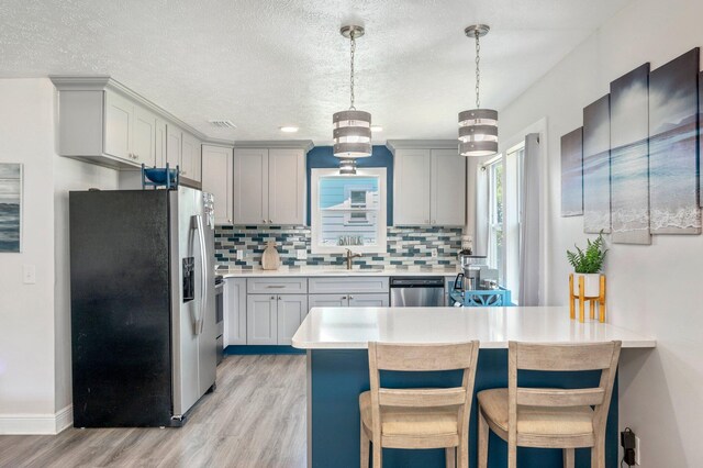 kitchen featuring decorative light fixtures, appliances with stainless steel finishes, backsplash, and light wood-type flooring