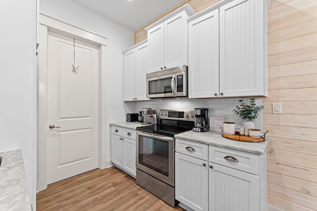 kitchen with light stone countertops, light wood-type flooring, tasteful backsplash, white cabinetry, and stainless steel appliances