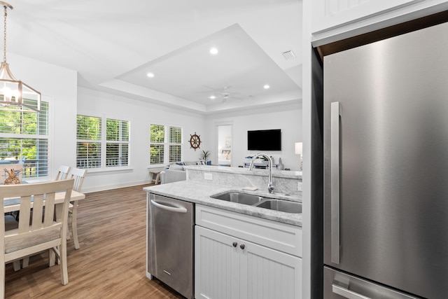 kitchen with sink, stainless steel appliances, a raised ceiling, white cabinets, and light wood-type flooring