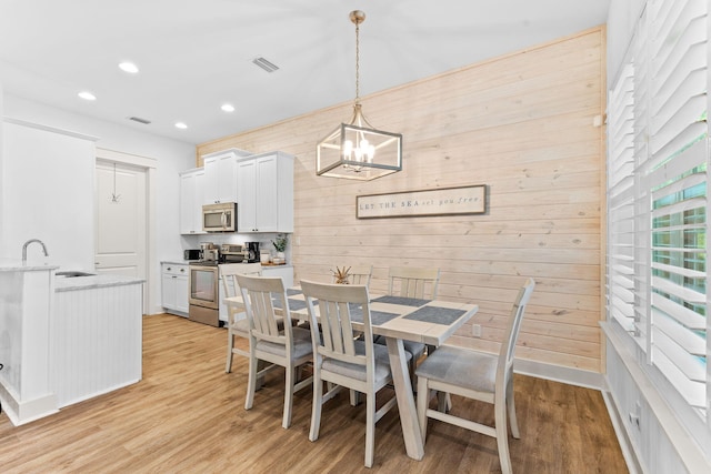 dining space featuring wooden walls, light hardwood / wood-style flooring, a notable chandelier, and sink