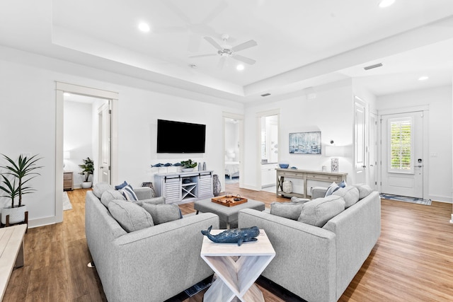 living room with ceiling fan, a tray ceiling, and light hardwood / wood-style flooring