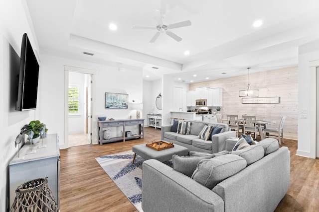 living room with a raised ceiling, light hardwood / wood-style flooring, ceiling fan, and wood walls