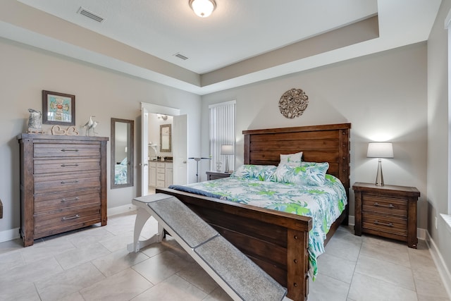 bedroom with a raised ceiling, connected bathroom, and light tile patterned flooring