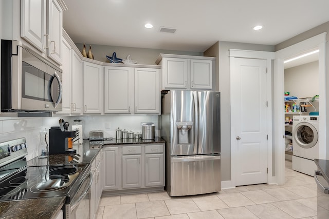 kitchen featuring washer / clothes dryer, white cabinetry, dark stone counters, and appliances with stainless steel finishes