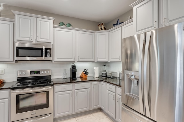 kitchen with backsplash, dark stone counters, appliances with stainless steel finishes, light tile patterned flooring, and white cabinetry