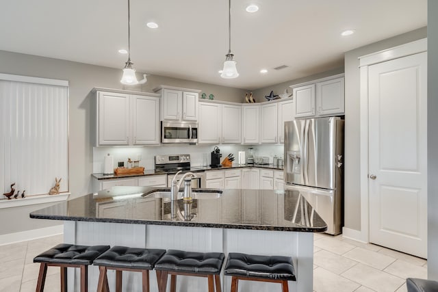 kitchen featuring a breakfast bar, light tile patterned flooring, an island with sink, and appliances with stainless steel finishes