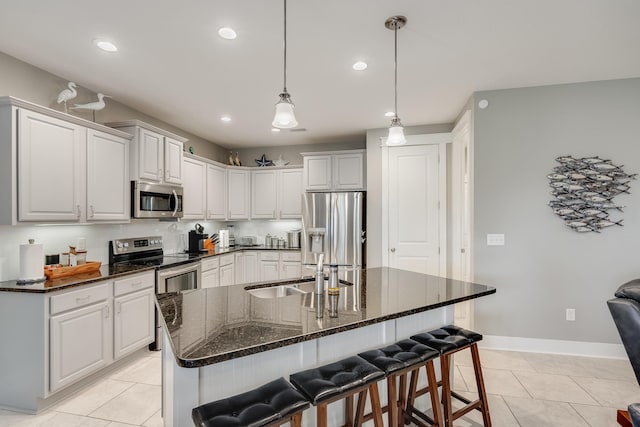 kitchen with pendant lighting, a kitchen island with sink, a breakfast bar area, light tile patterned floors, and stainless steel appliances