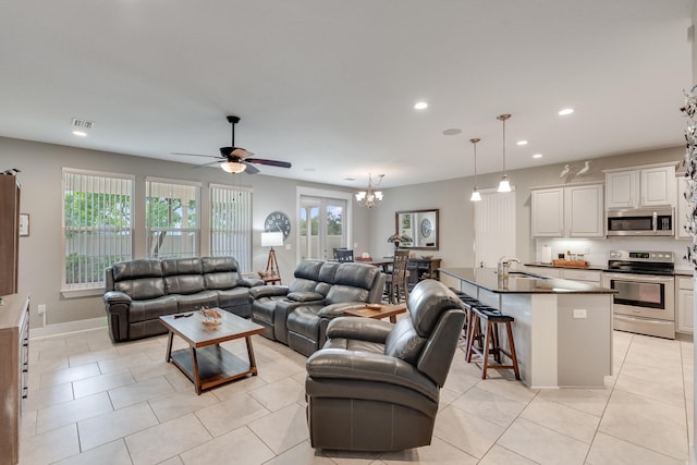 tiled living room featuring ceiling fan with notable chandelier and sink