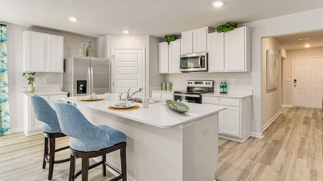 kitchen with a sink, white cabinetry, light countertops, appliances with stainless steel finishes, and a center island with sink