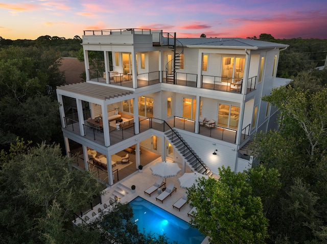 back house at dusk featuring a patio, a balcony, and an outdoor hangout area