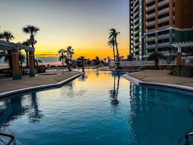 pool at dusk with a patio area, a pergola, and a community pool