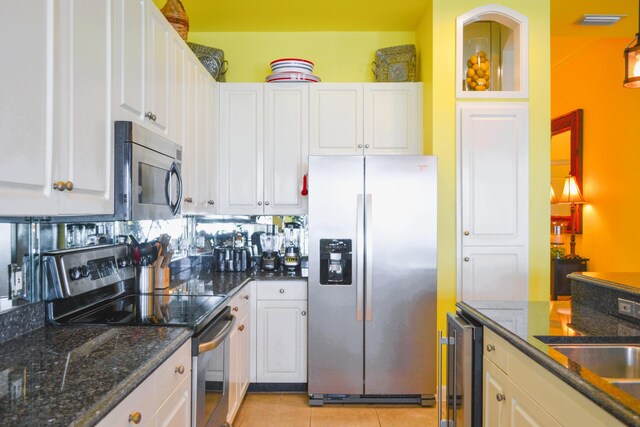 kitchen featuring light tile patterned floors, appliances with stainless steel finishes, dark stone countertops, and white cabinetry