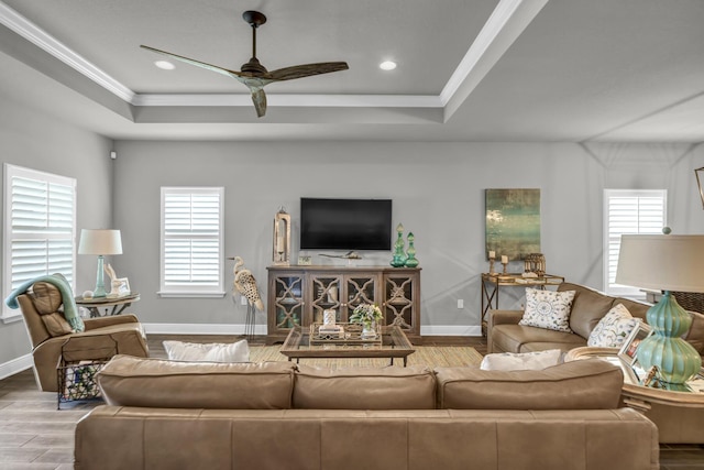 living room with wood-type flooring, a raised ceiling, ceiling fan, and a healthy amount of sunlight