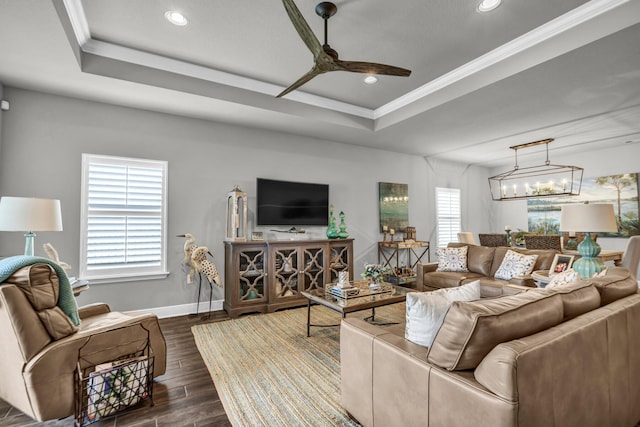 living room featuring ceiling fan with notable chandelier, a tray ceiling, and plenty of natural light