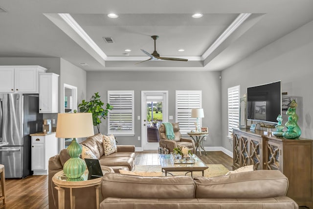 living room featuring a tray ceiling, ceiling fan, dark hardwood / wood-style floors, and ornamental molding