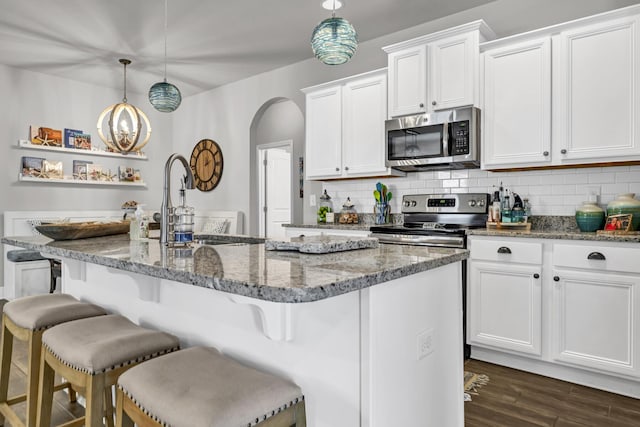 kitchen with light stone countertops, appliances with stainless steel finishes, decorative light fixtures, and a kitchen breakfast bar