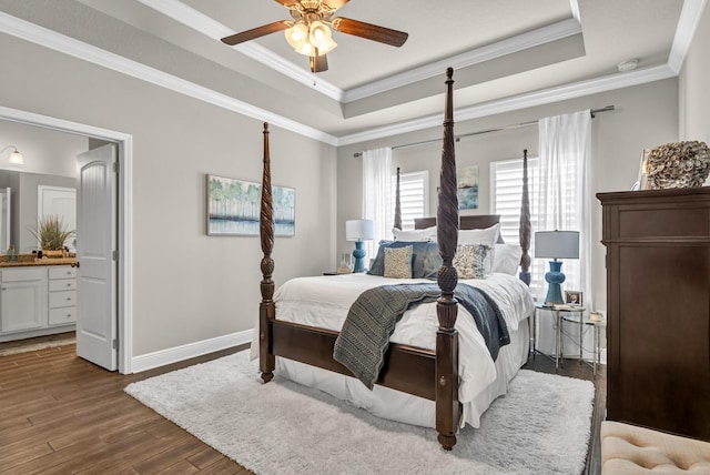 bedroom featuring dark hardwood / wood-style flooring, ensuite bathroom, ceiling fan, and a tray ceiling