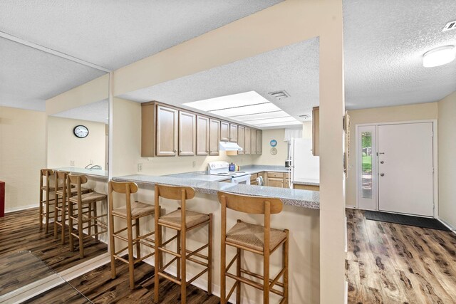 kitchen featuring a kitchen breakfast bar, kitchen peninsula, dark hardwood / wood-style flooring, and white appliances