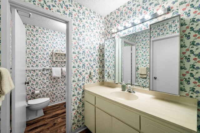 bathroom with hardwood / wood-style flooring, vanity, toilet, and a textured ceiling