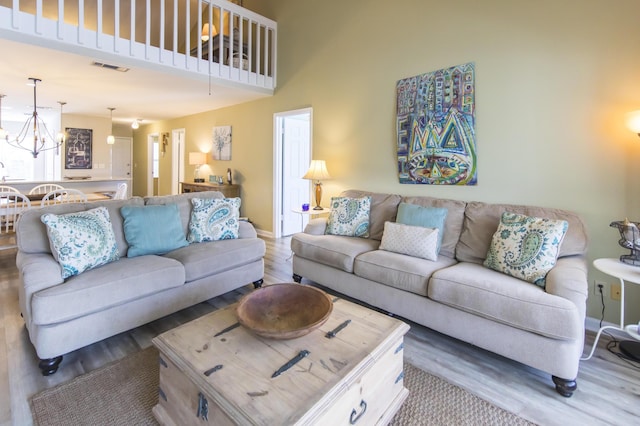 living room with a towering ceiling, light hardwood / wood-style floors, and a notable chandelier