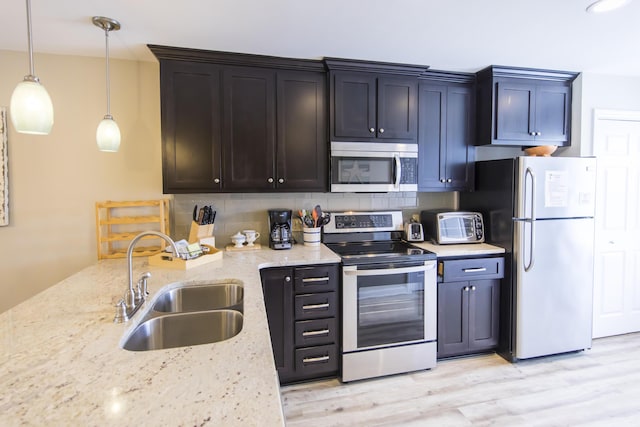 kitchen featuring sink, light stone countertops, hanging light fixtures, and appliances with stainless steel finishes