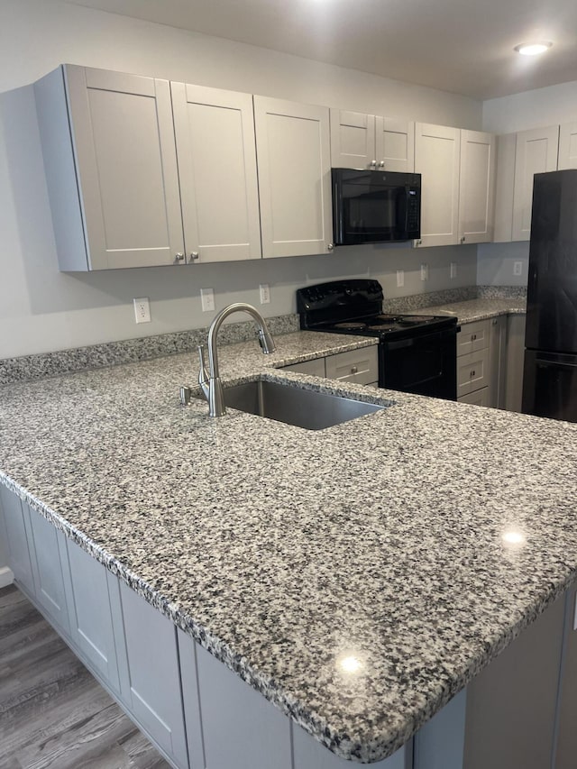 kitchen featuring kitchen peninsula, light stone countertops, black appliances, and light wood-type flooring