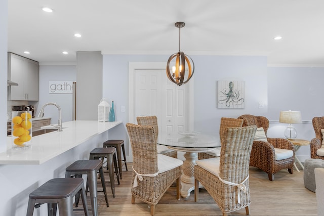 dining space featuring a notable chandelier, sink, light hardwood / wood-style flooring, and crown molding