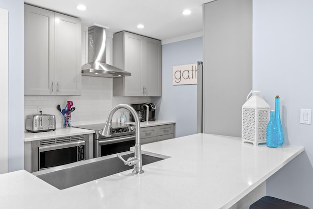 kitchen featuring wall chimney range hood, gray cabinetry, stove, tasteful backsplash, and stainless steel microwave