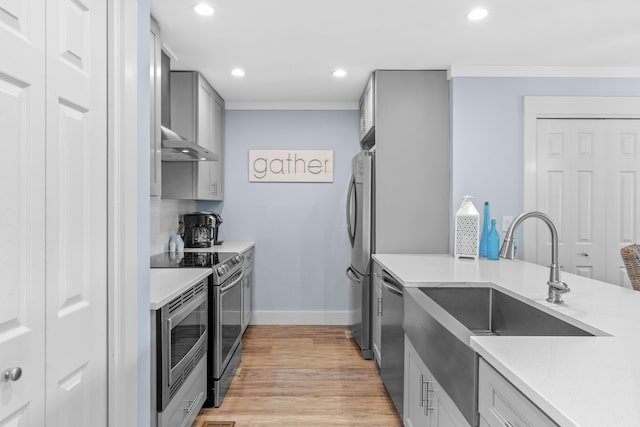 kitchen featuring stainless steel appliances, wall chimney range hood, light hardwood / wood-style flooring, and gray cabinets