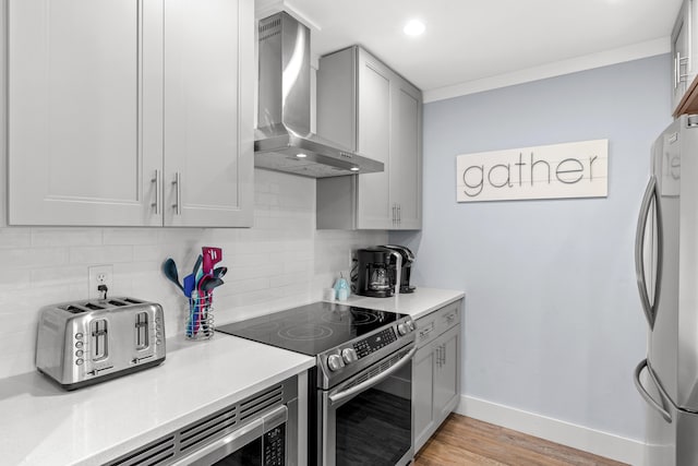 kitchen with wall chimney exhaust hood, tasteful backsplash, light wood-type flooring, and appliances with stainless steel finishes