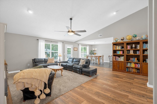 living room with a textured ceiling, high vaulted ceiling, wood-type flooring, and ceiling fan with notable chandelier