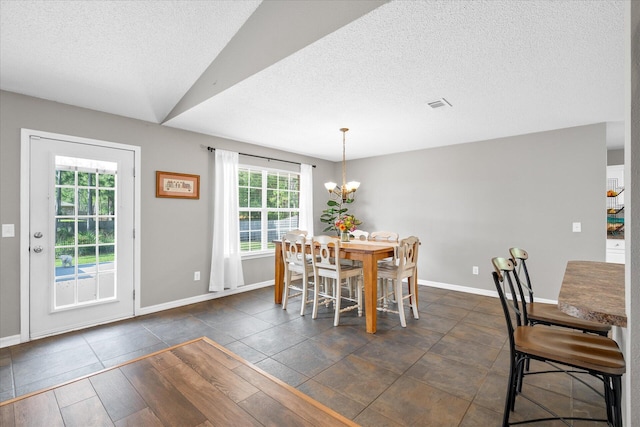 tiled dining space with a healthy amount of sunlight, lofted ceiling, a textured ceiling, and a chandelier