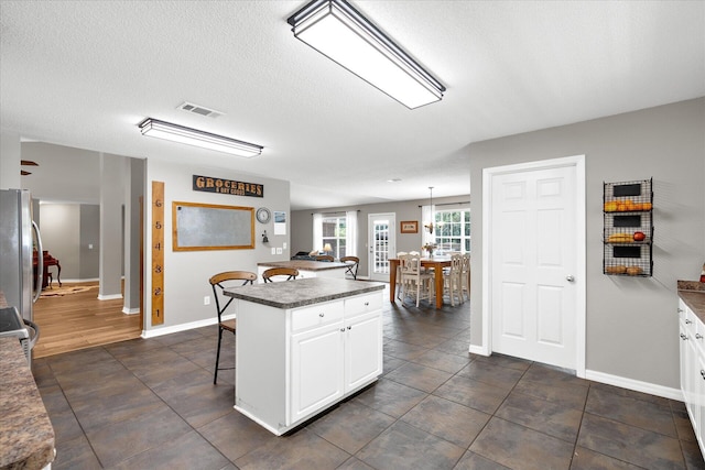 kitchen featuring stainless steel fridge, decorative light fixtures, a center island, white cabinetry, and a breakfast bar area