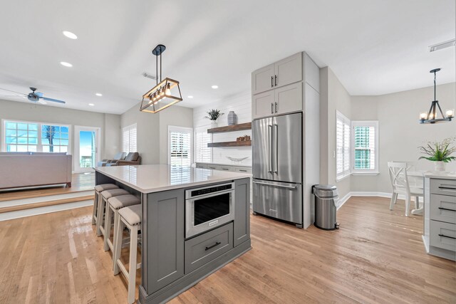 kitchen with a center island, gray cabinetry, ceiling fan with notable chandelier, light hardwood / wood-style flooring, and stainless steel appliances