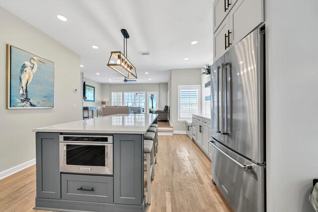 kitchen featuring hanging light fixtures, appliances with stainless steel finishes, light wood-type flooring, and a kitchen island