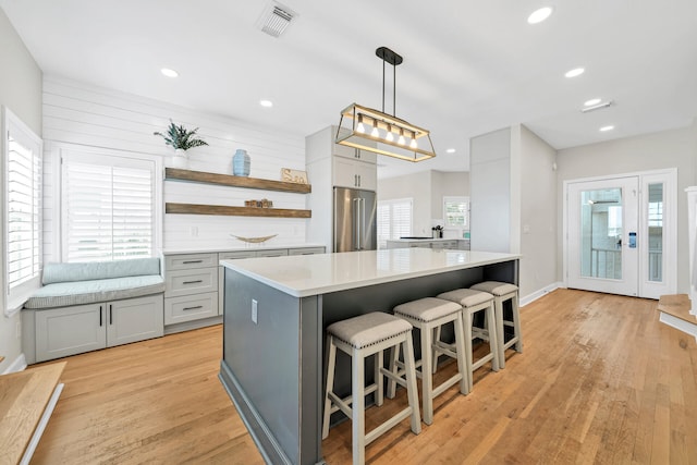 kitchen featuring a center island, high quality fridge, light hardwood / wood-style flooring, decorative light fixtures, and a kitchen bar