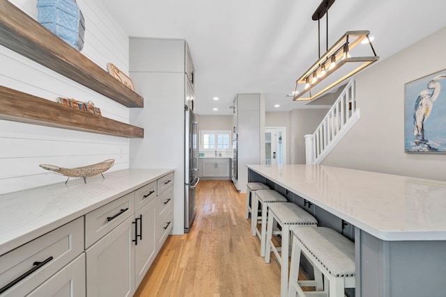 kitchen featuring decorative light fixtures, light stone counters, a kitchen bar, stainless steel fridge, and light wood-type flooring