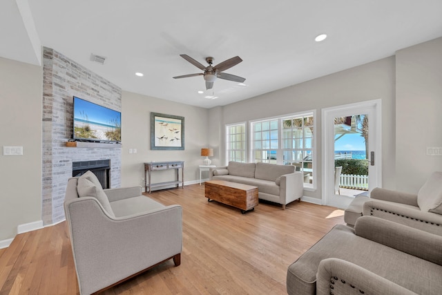 living room featuring ceiling fan, light wood-type flooring, and a fireplace