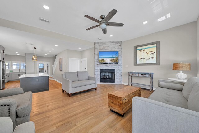 living room with ceiling fan, a fireplace, light wood-type flooring, and brick wall