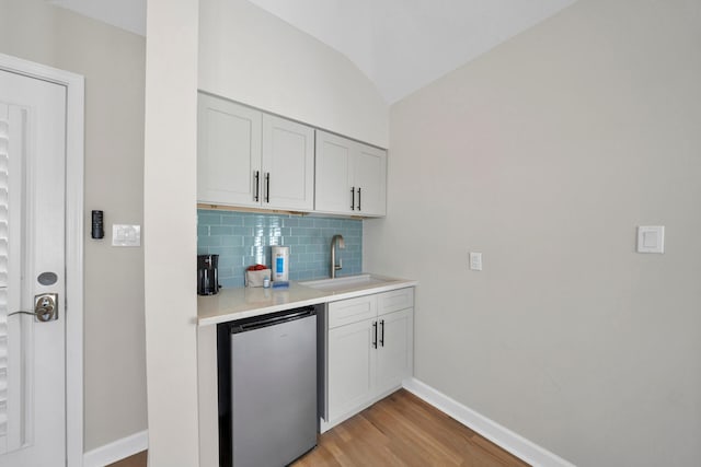 kitchen featuring light hardwood / wood-style flooring, vaulted ceiling, backsplash, sink, and white cabinetry