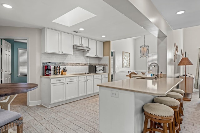 kitchen with white cabinets, sink, a skylight, an island with sink, and light hardwood / wood-style floors