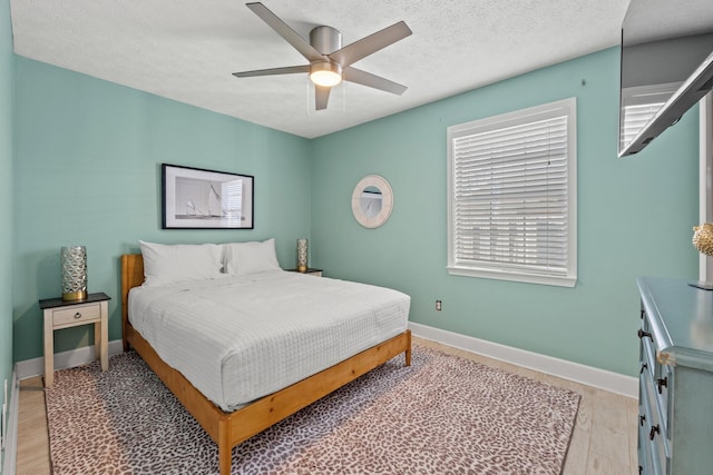 bedroom featuring multiple windows, a textured ceiling, light wood-type flooring, and ceiling fan