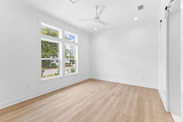 spare room featuring a barn door, ceiling fan, light hardwood / wood-style flooring, and a healthy amount of sunlight