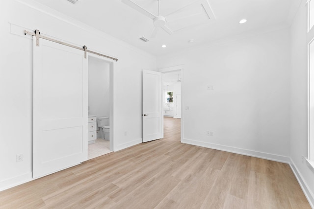 unfurnished bedroom with light wood-type flooring, ensuite bath, ceiling fan, crown molding, and a barn door