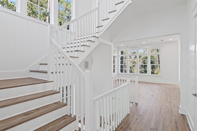 staircase with hardwood / wood-style flooring, high vaulted ceiling, and ceiling fan